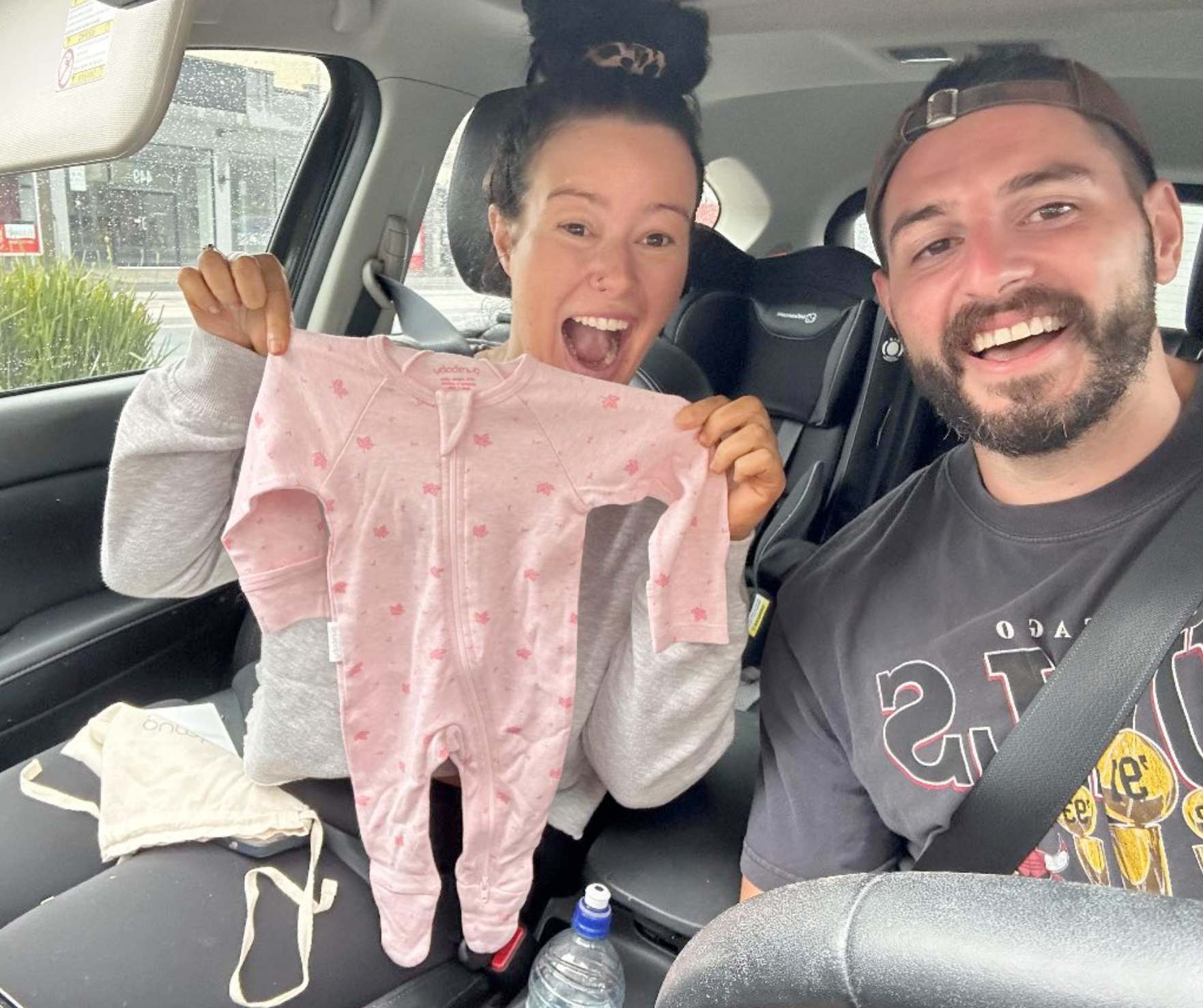 Becks At Home Insemination Success Story, Beck holding pink baby clothes next to her partner and both smiling